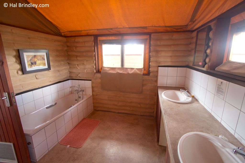 The spacious bathroom has two sinks, a tub, a shower, a toilet, and lovely artwork.