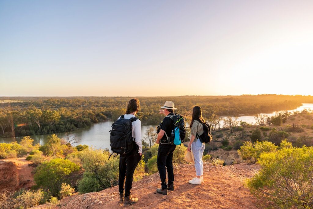 three people standing on a cliff and looking at river below